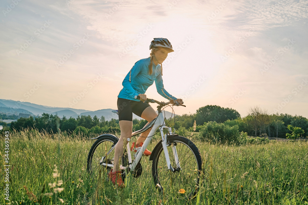 骑自行车的女人戴着头盔在阳光明媚的日子里在森林里的一座山上进行户外运动。Si
