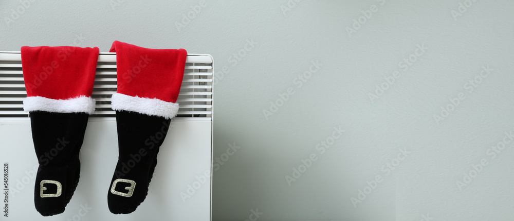 Baby Christmas clothes hanging on electric radiator near light wall with space for text