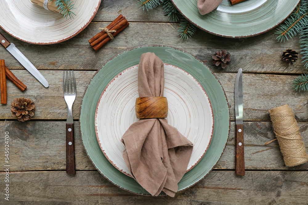 美丽的餐桌布置，木质背景上有圣诞树枝、冷杉锥和肉桂