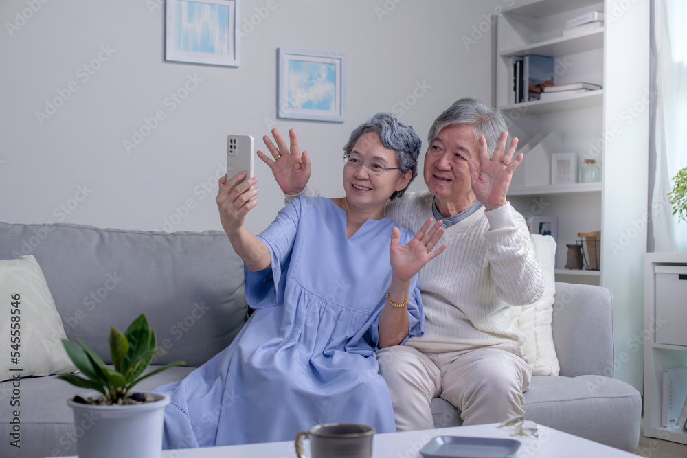 幸福的亚洲老年夫妇一起坐在家里客厅的沙发上微笑着