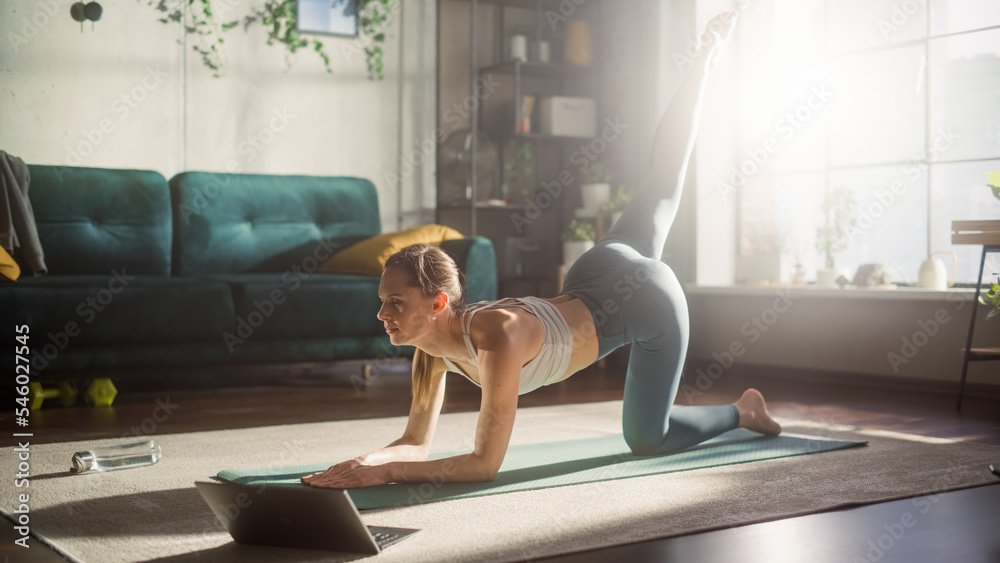 运动型年轻女性在笔记本电脑上观看训练视频时进行锻炼、拉伸和瑜伽