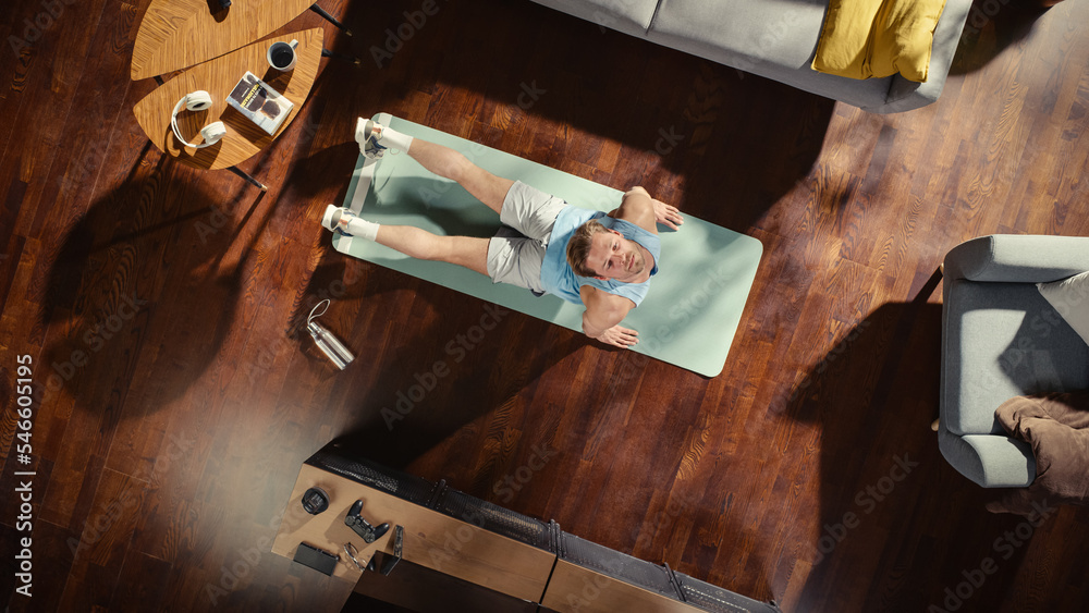 俯视运动：有魅力的家伙在家里的健身垫上做瑜伽拉伸。肌肉发达，英俊