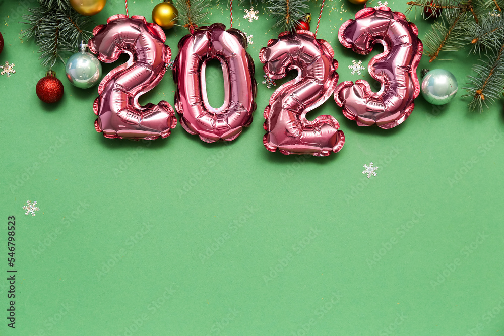 图2023由箔气球制成，绿色背景上有圣诞树枝和球