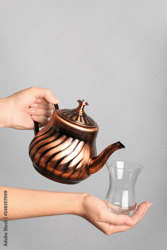 灰色背景下拿着土耳其茶壶和玻璃杯的女人
