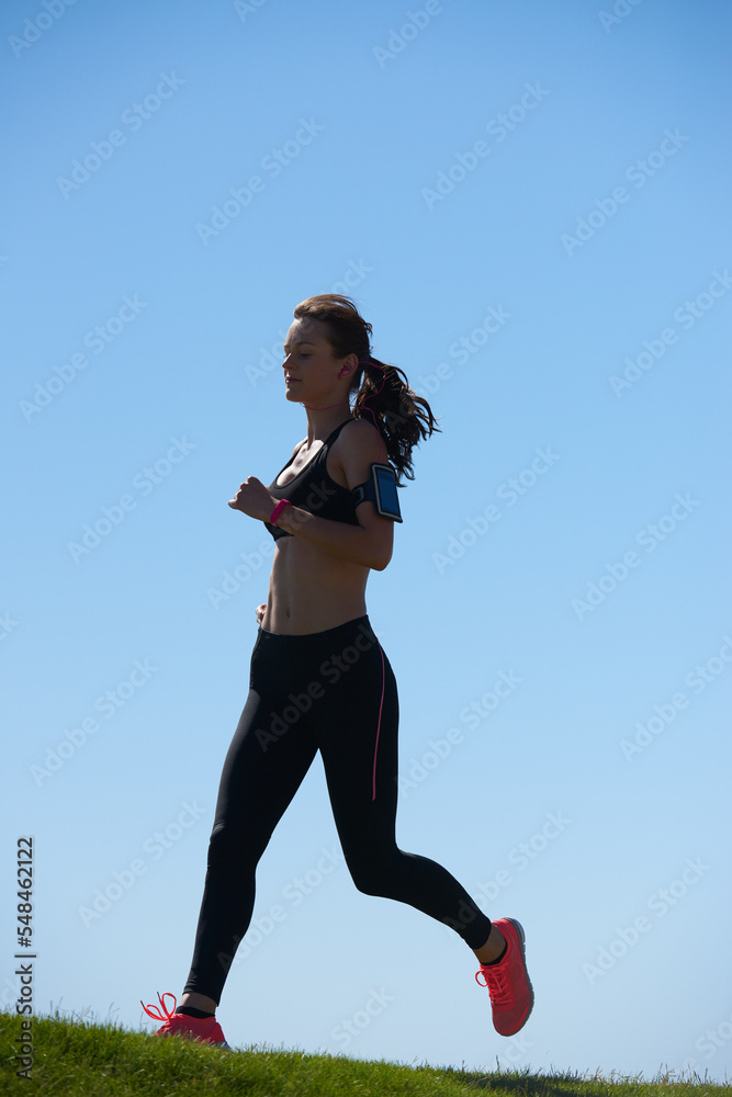 女性跑步者，草地和天空，在夏天、阳光下或户外为健身、健康和身心健康服务。运动员