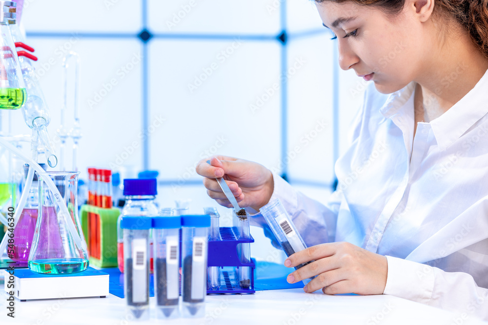 一名年轻的成年妇女在化学实验室对一家农业公司的土壤样本进行化学分析