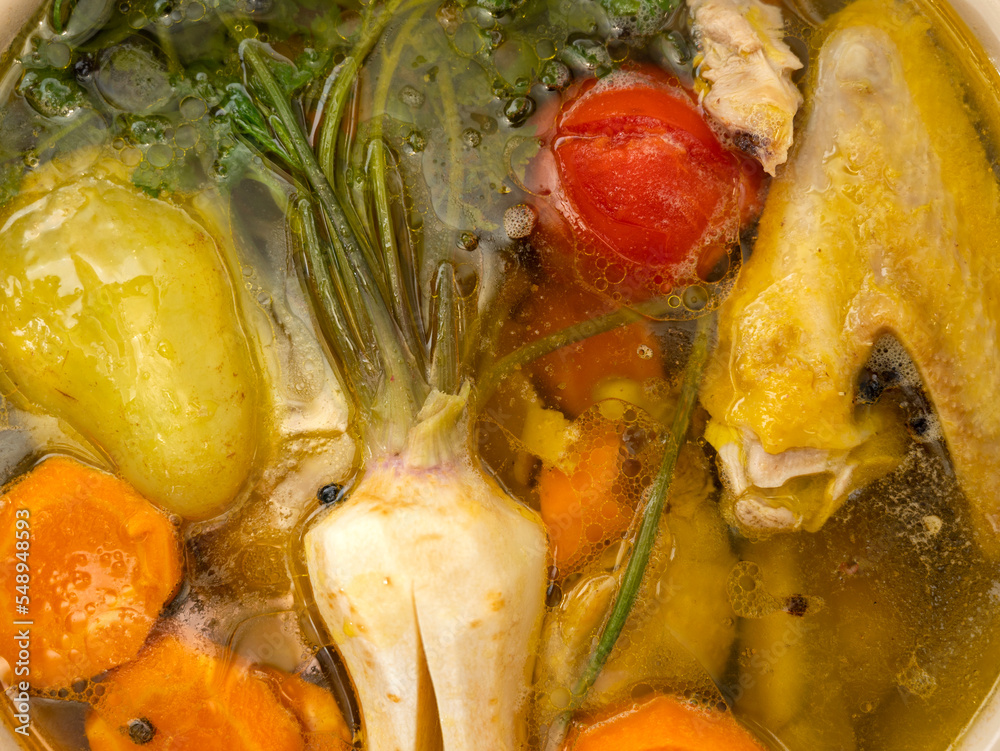 Chicken broth with pieces of meat on bone and vegetables in cooking pot
