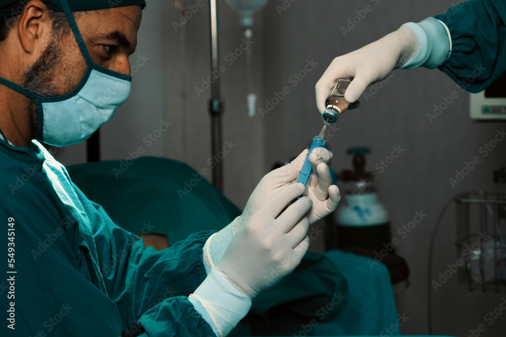 外科医生在无菌手术室辅助下从医用小瓶中填充注射器进行手术