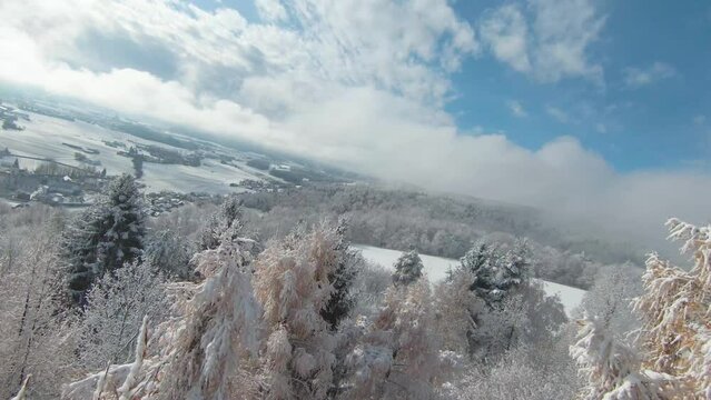 FPV DRONE: Beautiful hilly countryside and forest trees covered with early snow. Beginning of winter season with first snowfall. Snowy woodland area and gorgeous view over valley in late autumn snow.