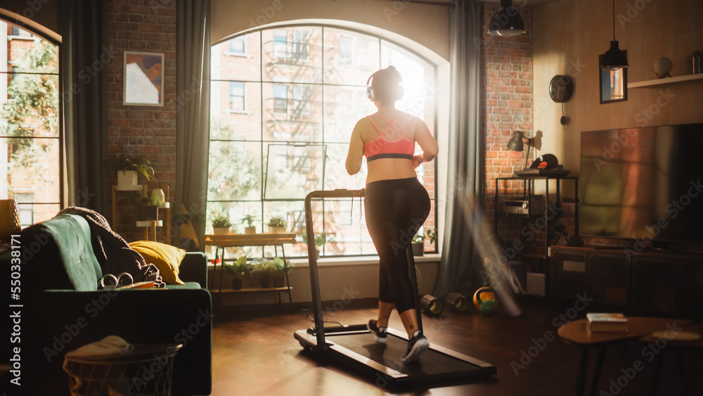 美丽的运动加大号身材积极的运动女性在家健身房的跑步机上跑步。Ener