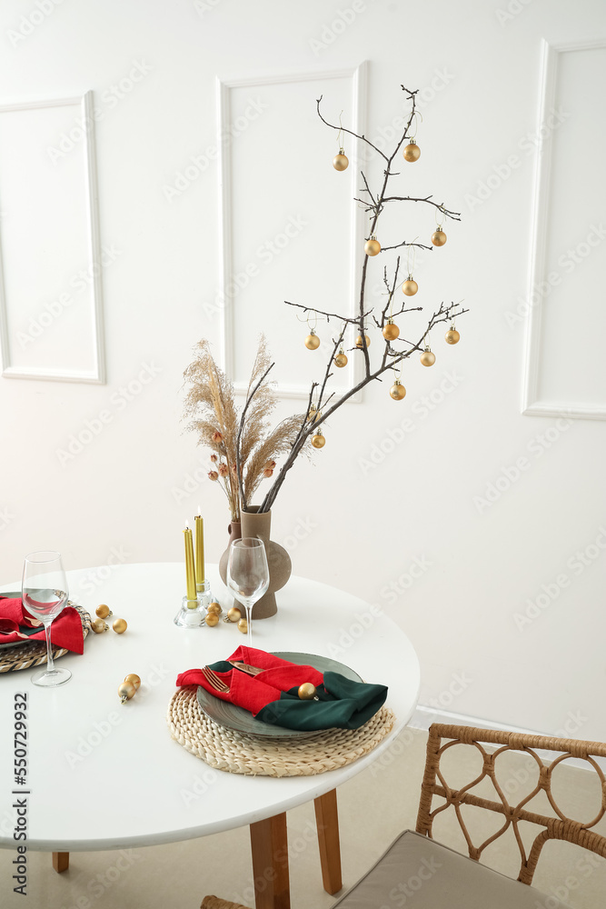 Vases with tree branches, pampas grass and Christmas balls on dining table in room