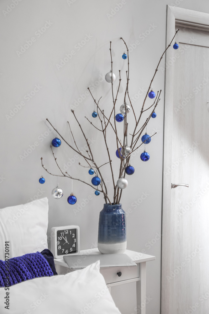 Vase with tree branches, Christmas balls and clock on table in bedroom