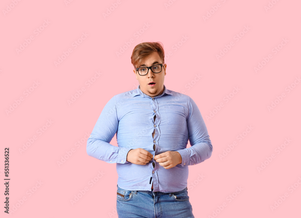 Young overweight man in tight shirt on pink background