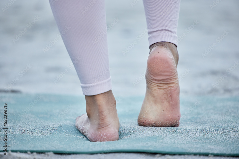 瑜伽女性在海滩上伸展双脚，进行整体足部锻炼或nat锻炼