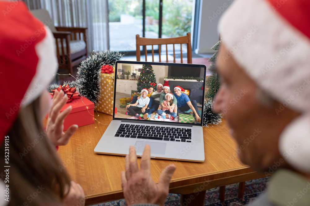 戴着圣诞老人帽的高加索父女在圣诞笔记本电脑上与高加索家庭视频通话