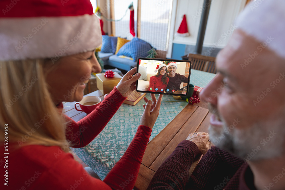 Caucasian couple with santa hats having christmas video call with happy caucasian couple
