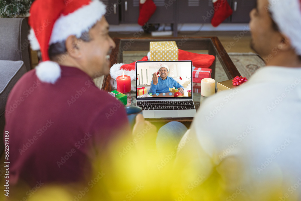 戴着圣诞老人帽的混血父亲和成年儿子与快乐的混血男子视频通话