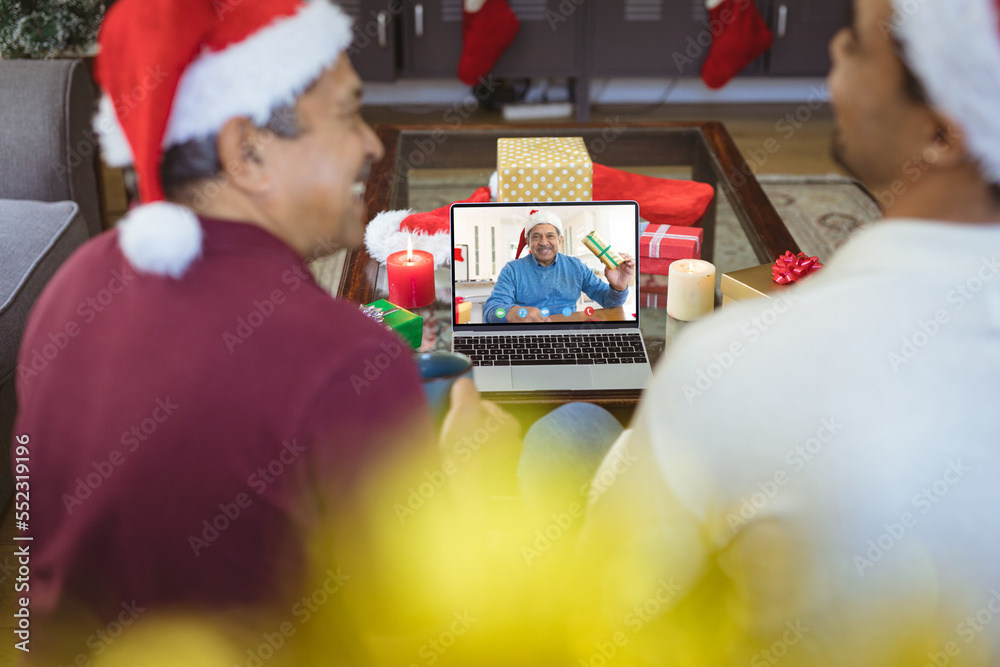 Biracial father and adult son with santa hats having video call with happy biracial man