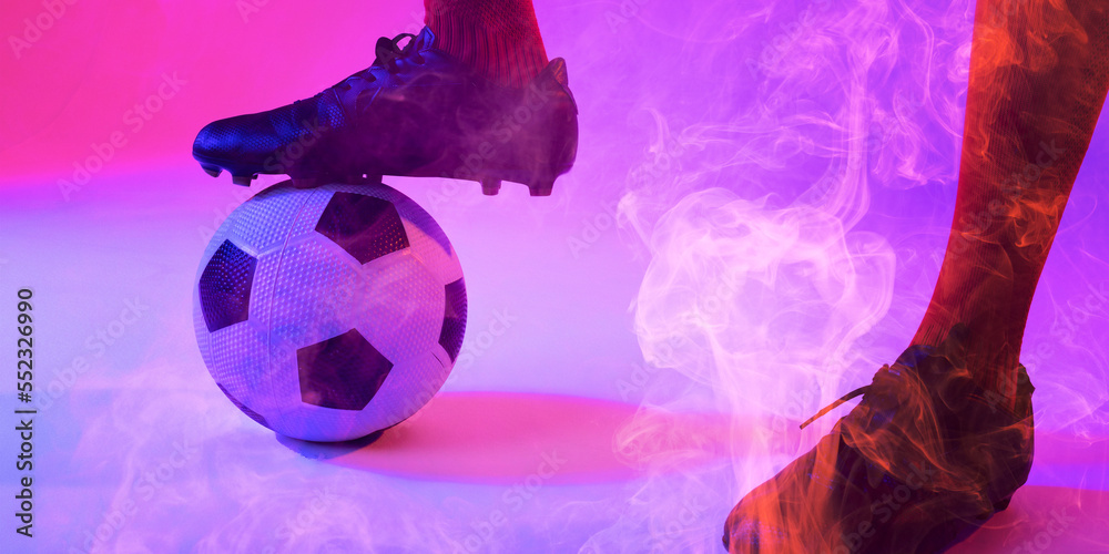 Low section of male player wearing black sport shoes with leg on ball against colorful smoke
