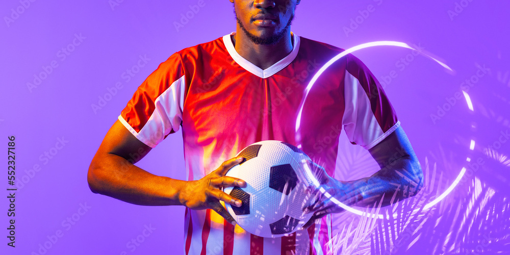 Midsection of african american male player holding ball by illuminated plants and circle