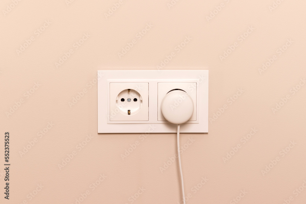 Group of white european electrical outlets with round plug inserted into it on modern beige wall