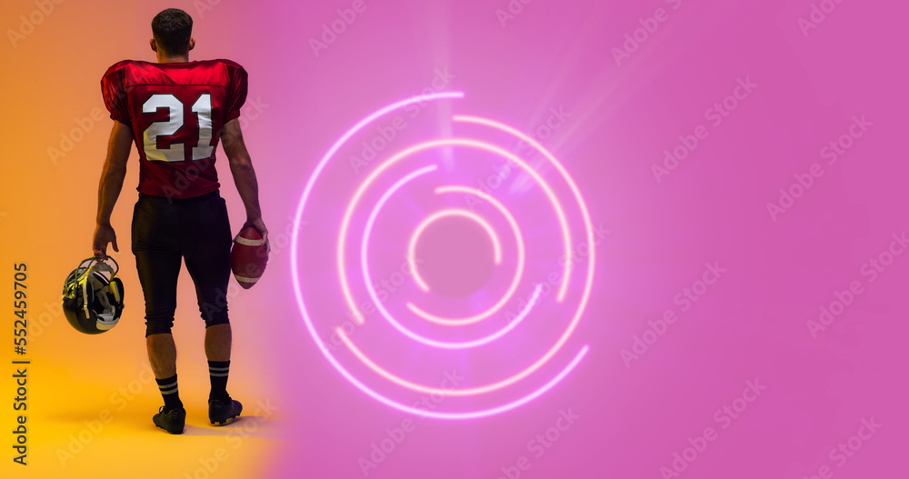照明圆形结构下美国足球运动员持球和头盔的后视图