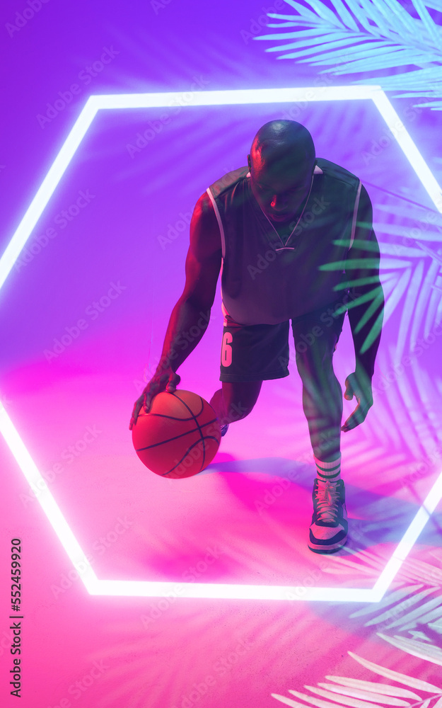 African american bald basketball player juggling with ball by illuminated hexagon and plants
