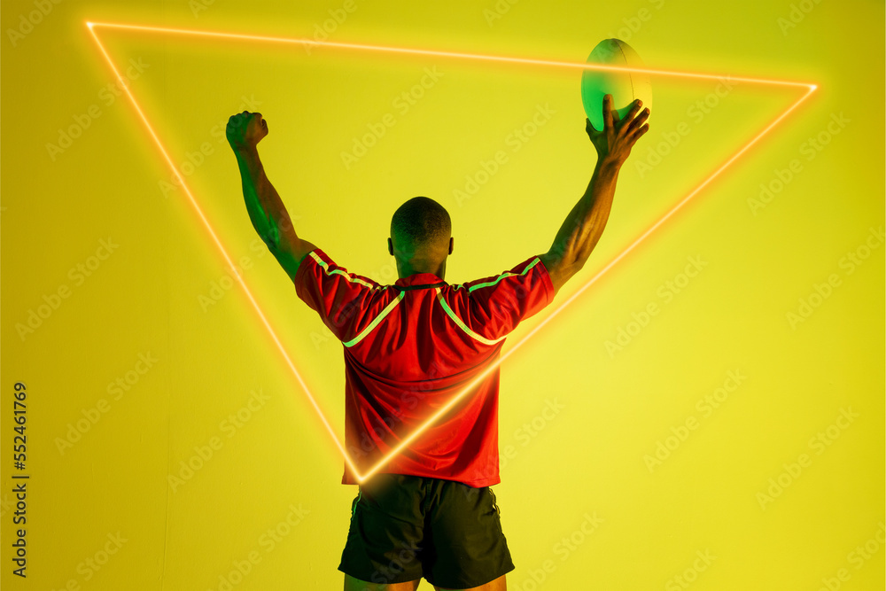 三角形霓虹灯笼罩着非洲裔美国橄榄球运动员，在黄色背景上举起双臂拿球