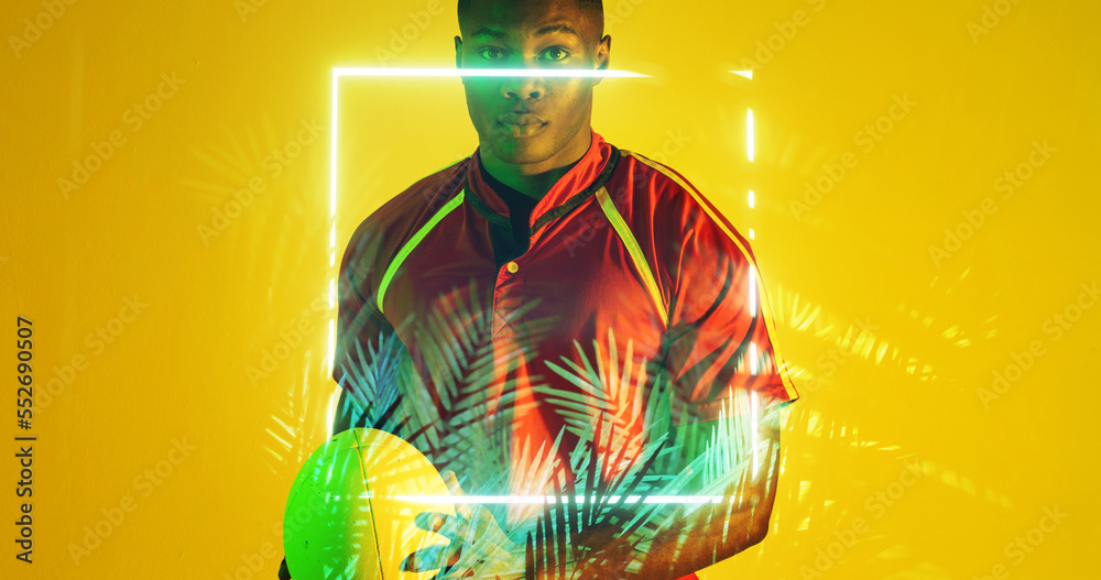 Portrait of african american rugby player with ball by glowing square and plant on yellow background