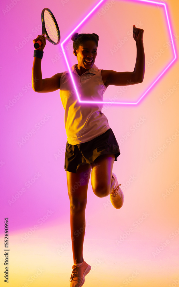 Excited african american tennis player holding racket and raising hands by illuminated hexagon
