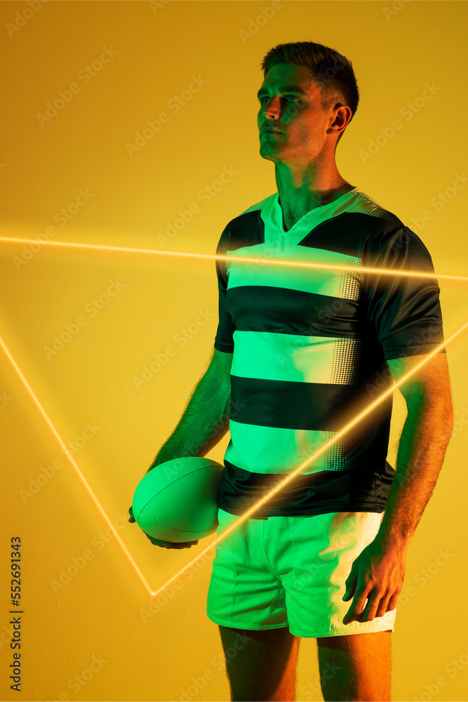 白人男子橄榄球运动员拿着球，站在黄色背景的发光三角形旁