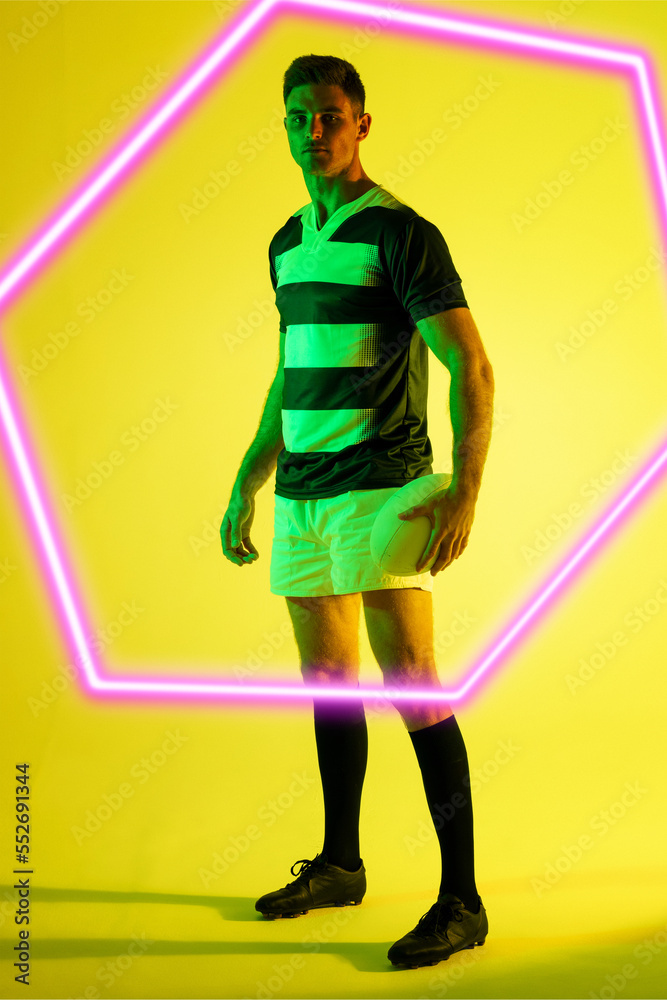 高加索男子橄榄球运动员，站着球，黄色背景上有发光的六边形