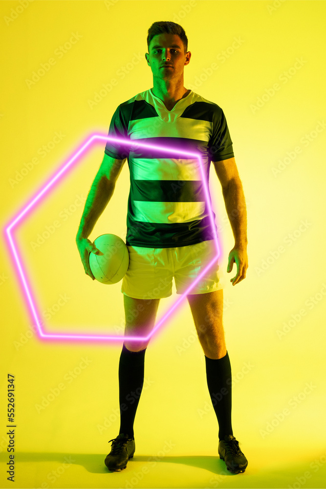 严肃的白人男性橄榄球运动员，站在黄色背景上，用发光的三角形拿球