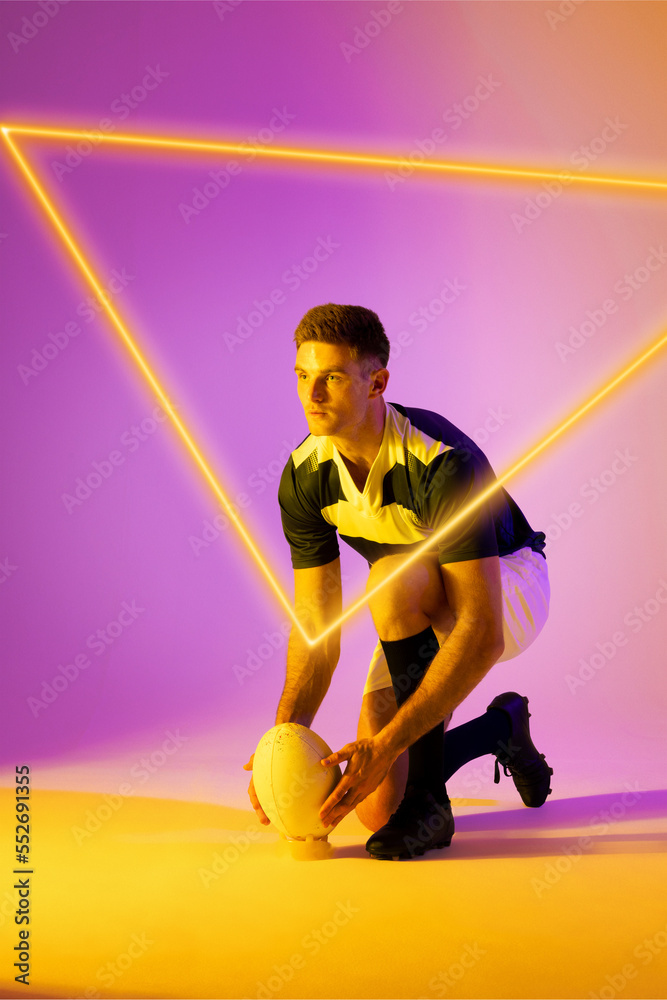 高加索男子橄榄球运动员将球放在渐变背景上的照明三角形上