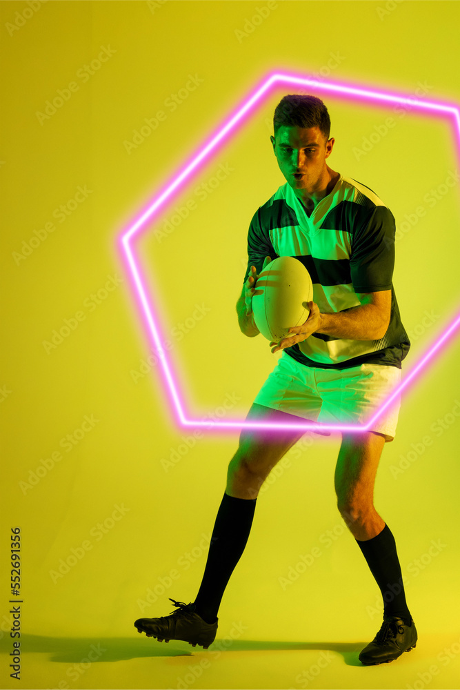 Full length of caucasian male rugby player with ball by illuminated hexagon on yellow background