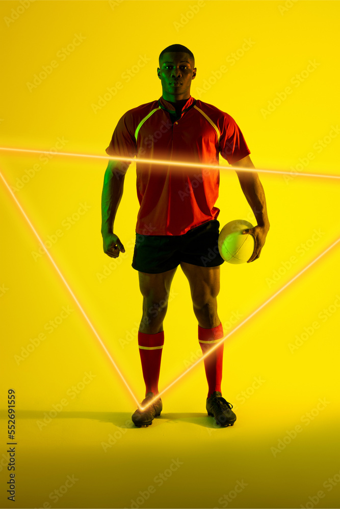 Confident african american male player with rugby ball by illuminated triangle on yellow background
