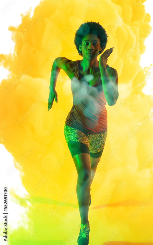African american female athlete with afro hair running over yellow smoky background, copy space