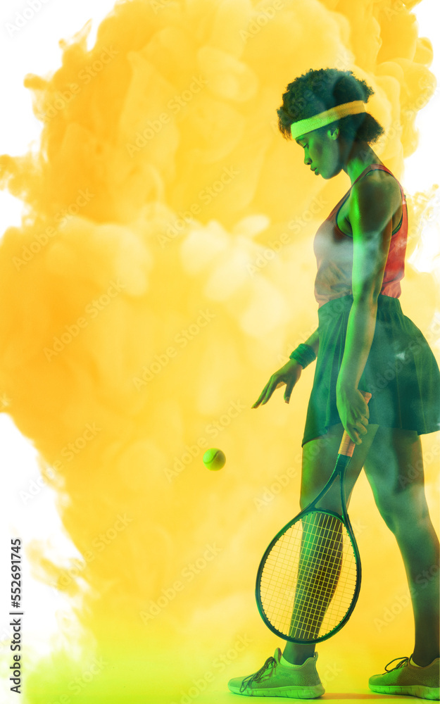 非裔美国女网球运动员在黄色烟雾背景下拿着球和球拍的侧视图
