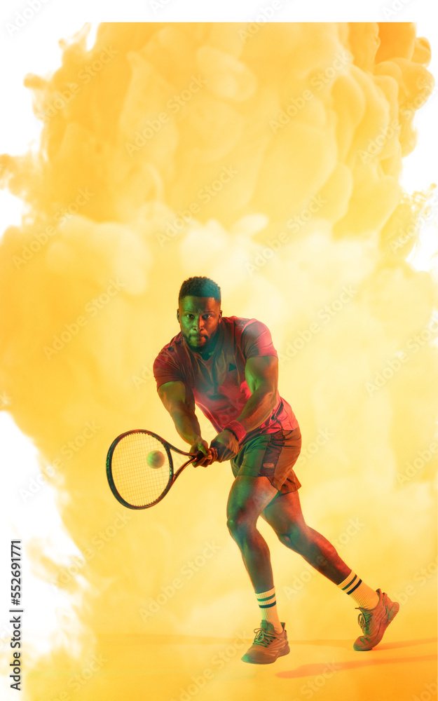 Full length of african american male player playing tennis with racket over yellow smoky background