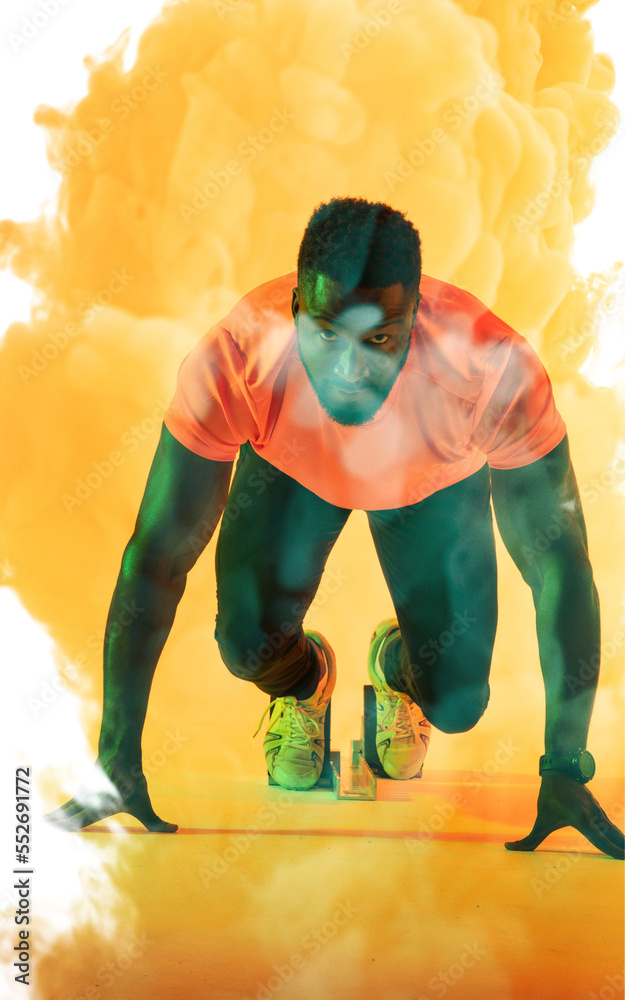 在黄色烟雾背景下，自信的非裔美国男运动员站在起跑位置