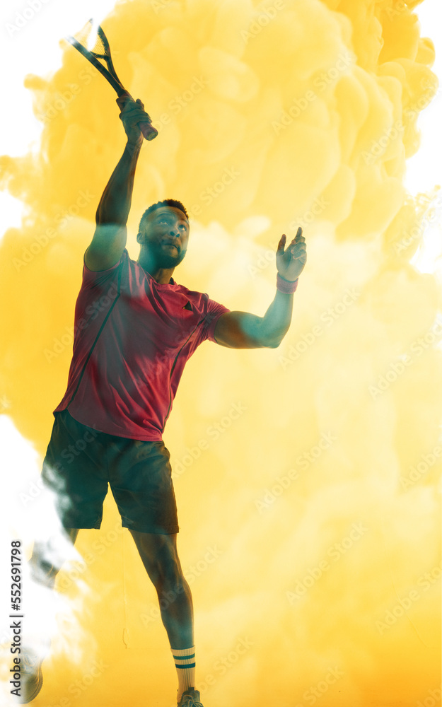 African american male tennis player hitting with racket over yellow smoky background