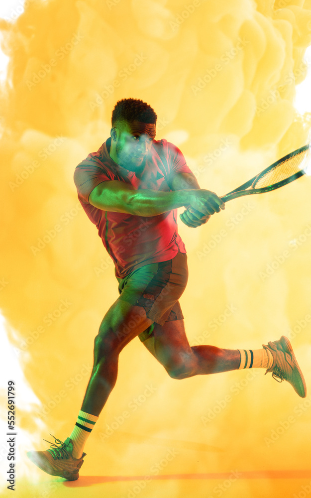 African american male tennis player hitting with racket against smoky yellow background