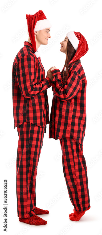Young couple in Santa hats and pajamas holding hands on white background