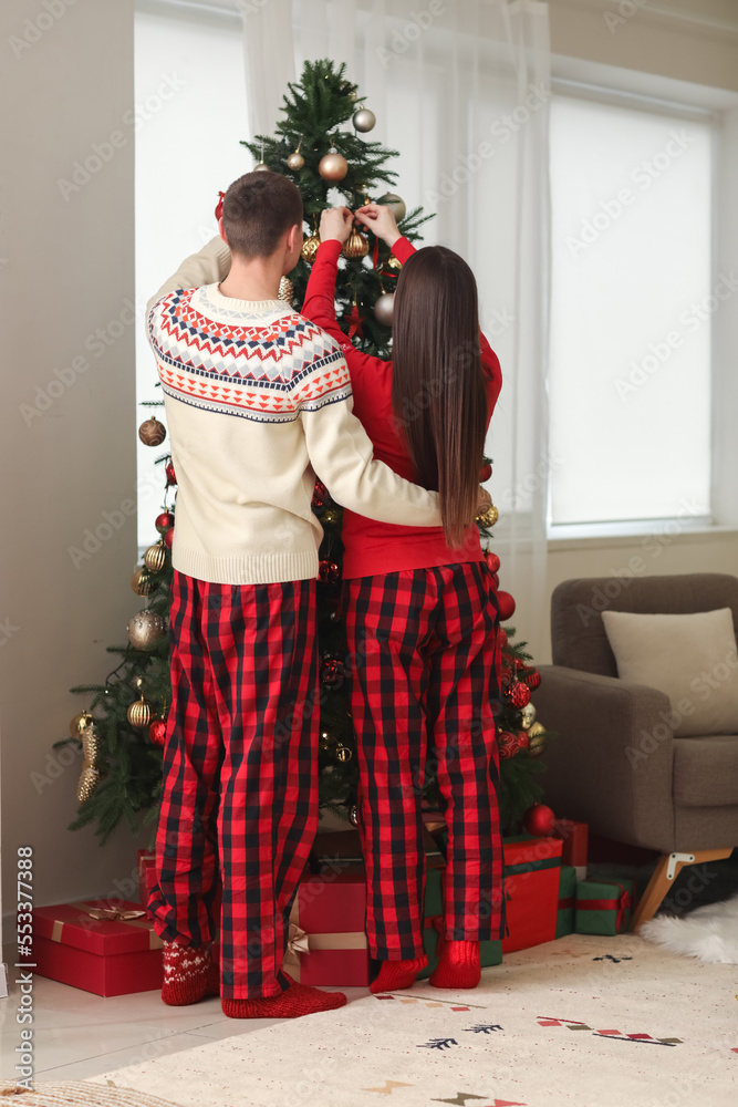 穿着睡衣的年轻夫妇在家装饰圣诞树，后视图