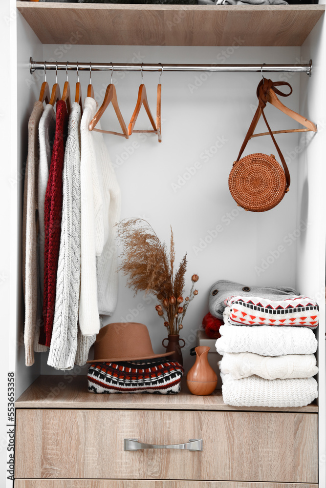 Warm knitted sweaters, hat, bag and vases on shelf in wardrobe