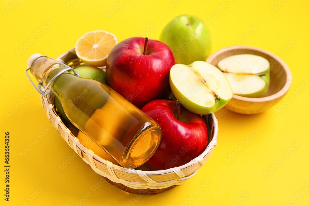 篮子里装着一瓶苹果醋和黄色背景的水果