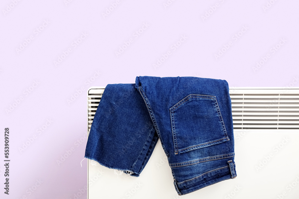 牛仔裤在淡紫色墙壁附近的电散热器上烘干，特写