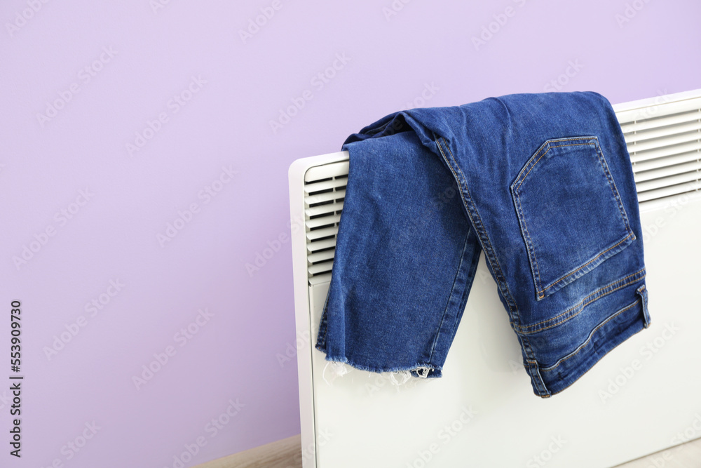 牛仔裤在淡紫色墙壁附近的电散热器上烘干，特写