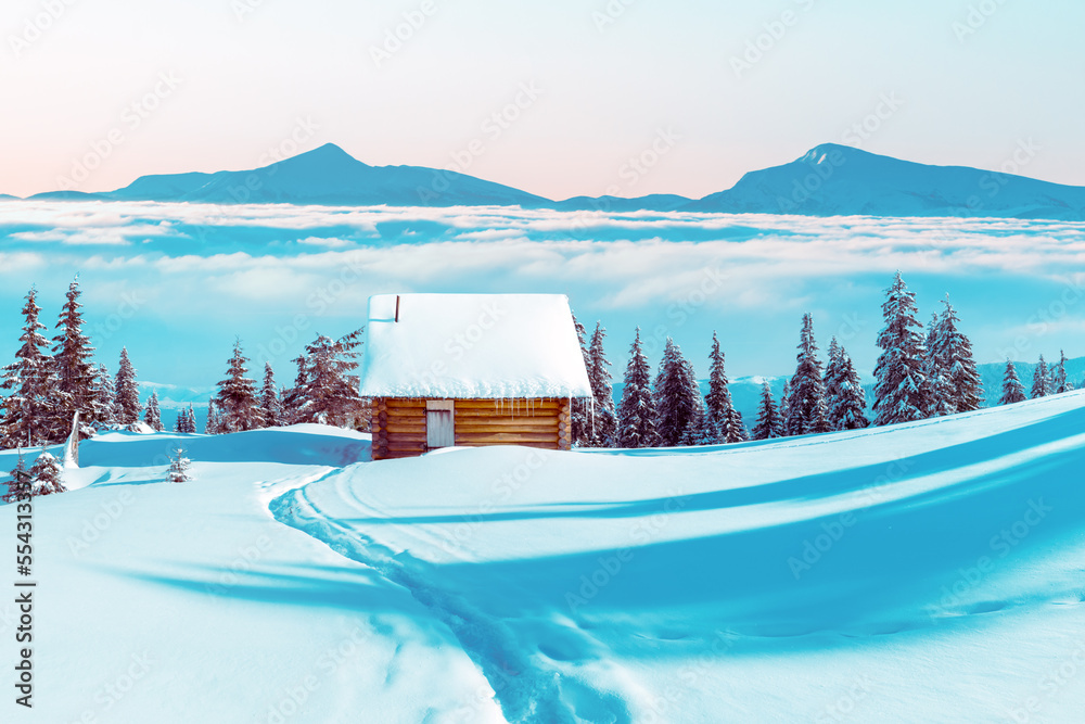 Fantastic winter landscape with wooden house and mountain peaks in mist in snowy mountains. Christma
