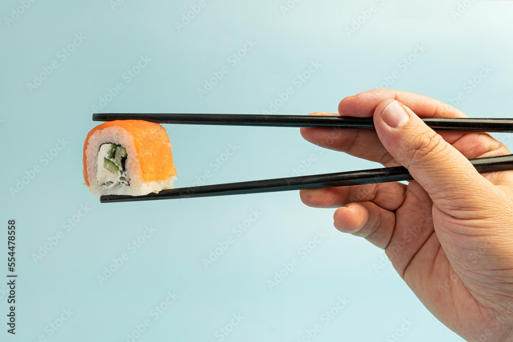 餐厅顾客手里拿着黑色筷子的寿司卷特写